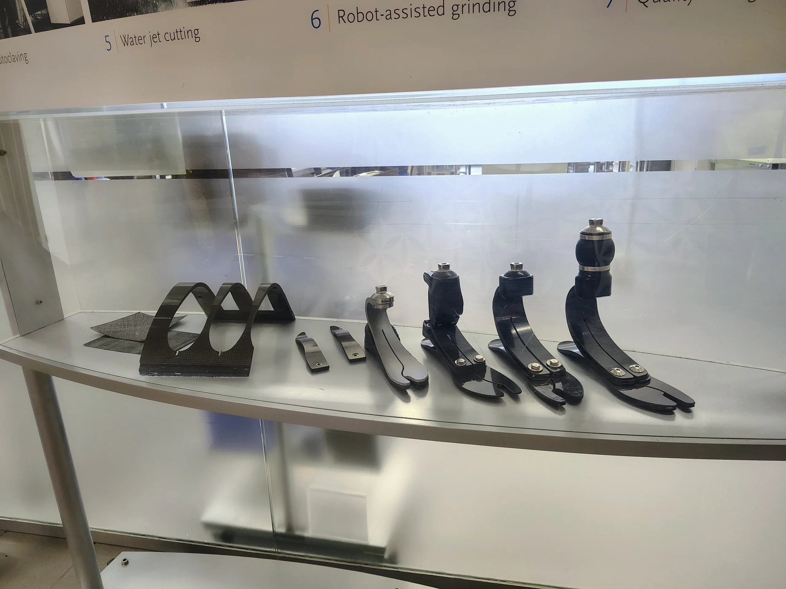 Display showing carbon-fiber prosthetic foot components at several stages of manufacturing, from unfinished carbon structures to completed foot assemblies.