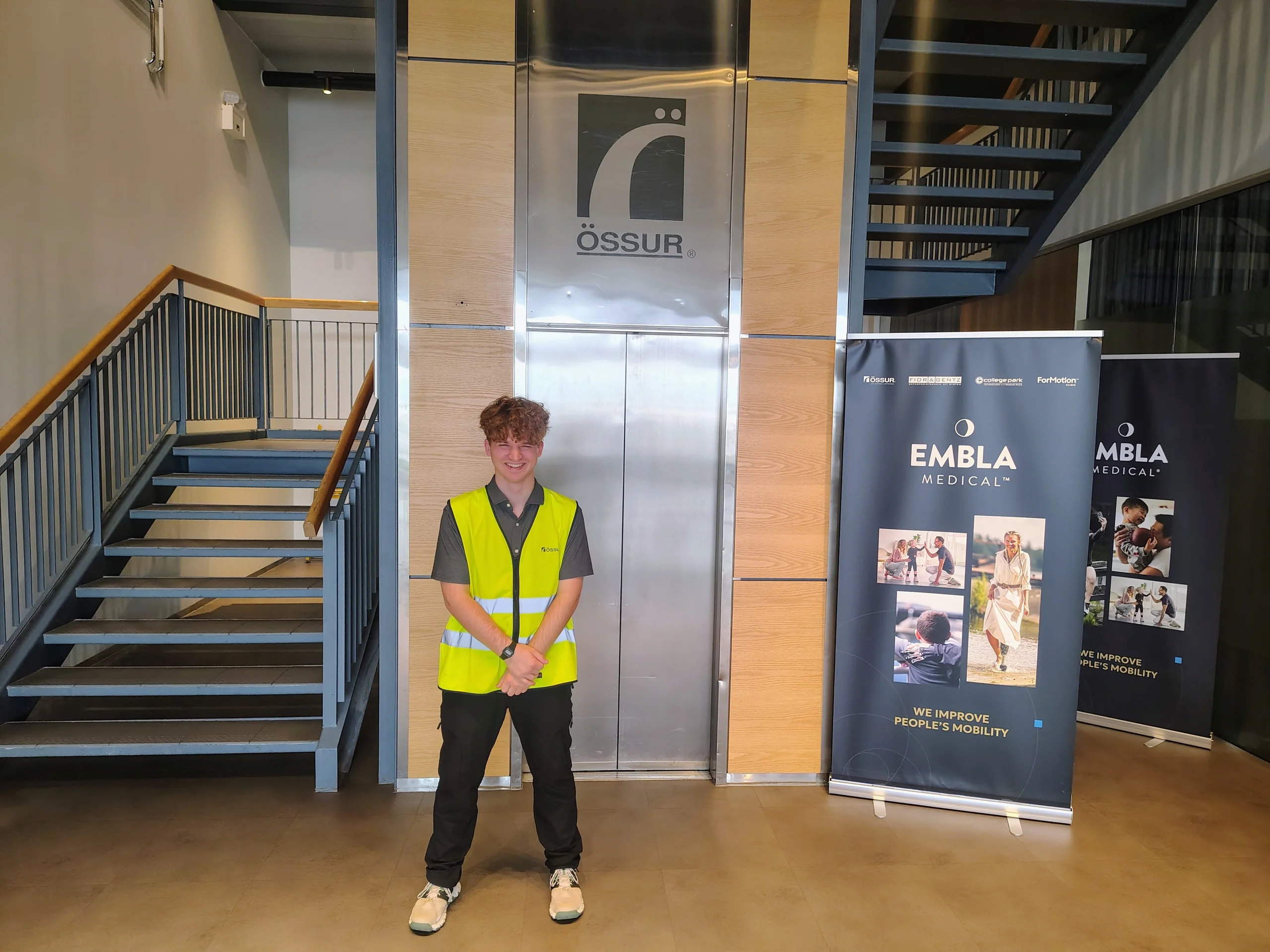 Andrew standing inside Össur headquarters in Reykjavík beside Össur signage.