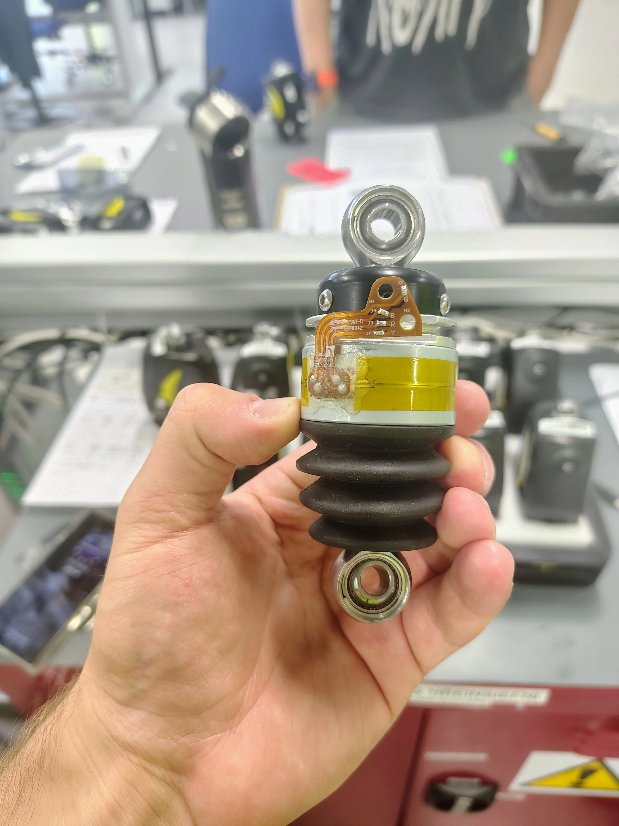 Internal Proprio Foot actuator held in a person's hand, showing its bearings, electronics, cylindrical housing, and black flexible bellows.