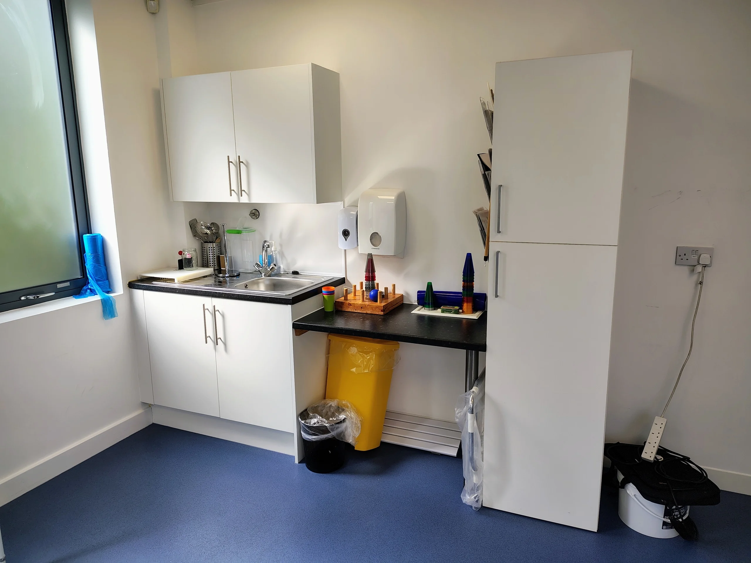 Kitchen area with a sink, countertop, cabinets and household items at the clinic.
